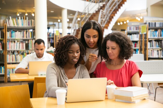 Lächelnde Frauen, die mit Laptop an der öffentlichen Bibliothek arbeiten