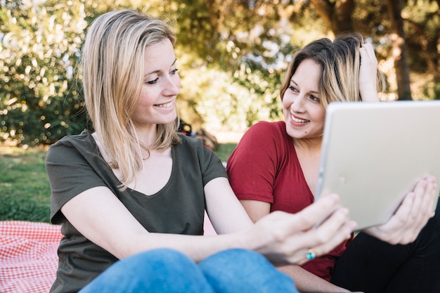 Kostenloses Foto lächelnde frauen, die tablette im park durchstöbern