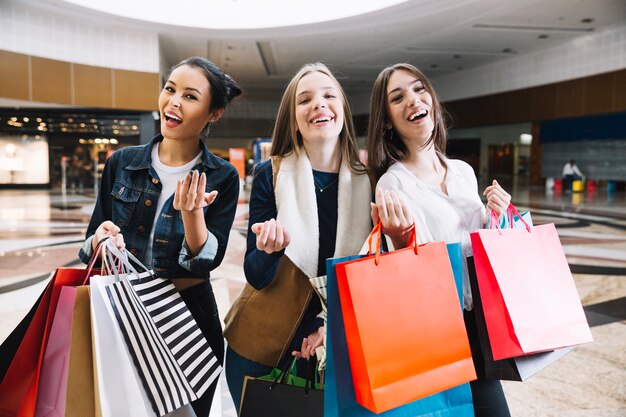 Lächelnde Frauen mit Taschen gestikulieren in die Kamera