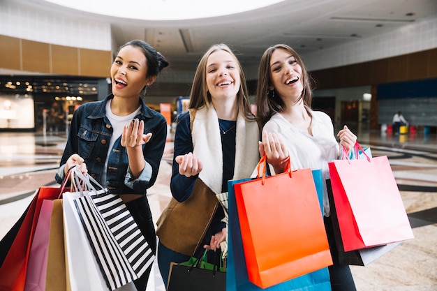 Lächelnde Frauen mit Taschen gestikulieren in die Kamera