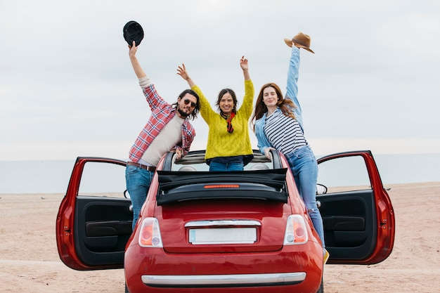 Lächelnde Frauen nähern sich Mann mit den angehobenen Händen, die heraus vom Auto auf Ufer sich lehnen