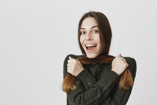 Lächelnde fröhliche brünette Frau, die mit Haaren spielt und lacht