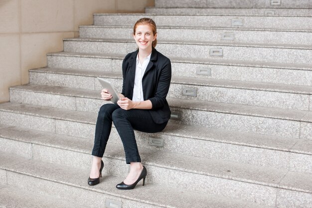 Lächelnde Geschäftsfrau, die Tablette auf Treppe verwendet