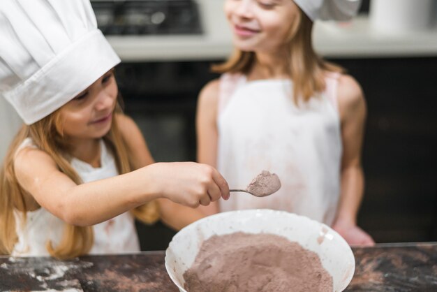 Lächelnde Geschwister im tragenden Hut des Küchenchefs, der Löffel des Kakaopulvers nimmt