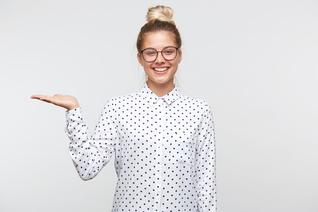 Kostenloses Foto lächelnde glückliche junge blonde frau in guter laune steht, gekleidet in ein weißes hemd mit schwarzen tupfen