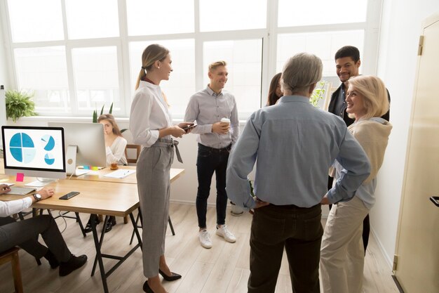 Lächelnde glückliche junge und ältere Büroangestellte, die beim Coworking sprechen