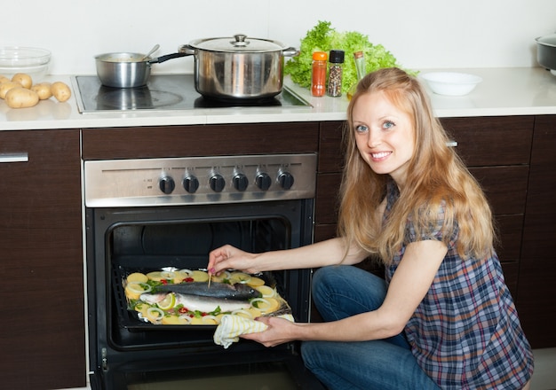 Kostenloses Foto lächelnde hausfrau kochen salzwasser fisch und kartoffeln auf blatt pfanne