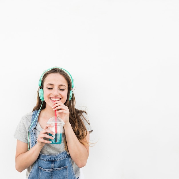 Lächelnde hörende Musik der jungen Frau auf Kopfhörer genießen, Saft über weißem Hintergrund zu trinken
