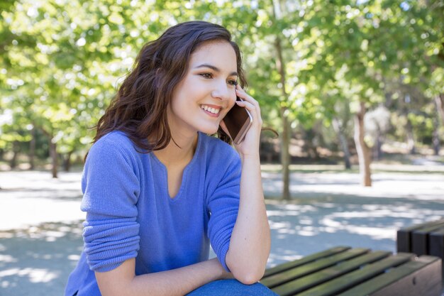 Lächelnde hübsche Frau, die am Handy im Park plaudert