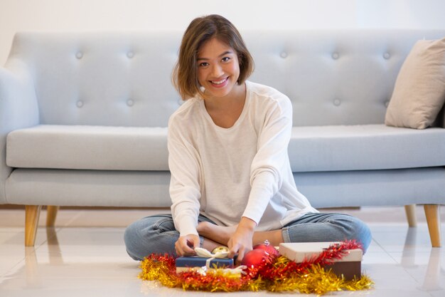 Lächelnde hübsche Frau, die auf Fußboden mit Weihnachtsgeschenken sitzt