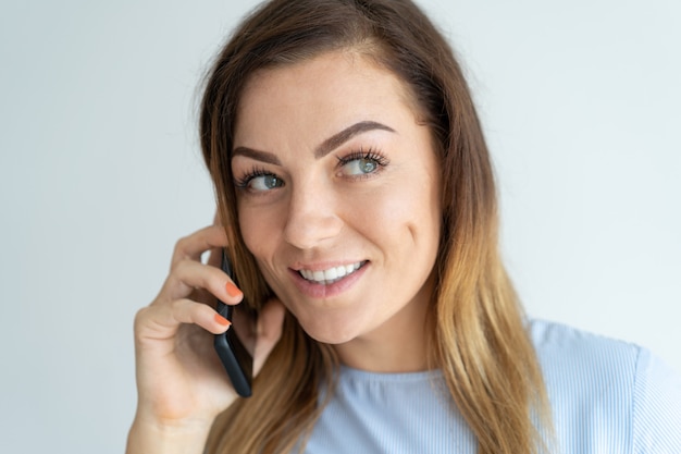 Lächelnde hübsche Frau, die auf Smartphone spricht. Positive Dame, die um Handy ersucht.