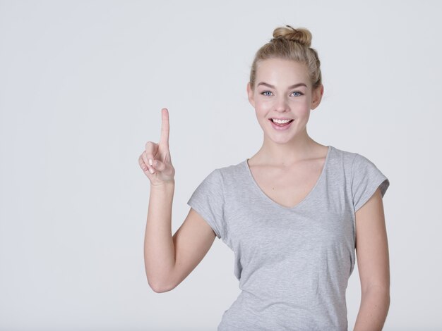 Kostenloses Foto lächelnde hübsche frau, die finger über grauem hintergrund zeigt. kamera betrachten