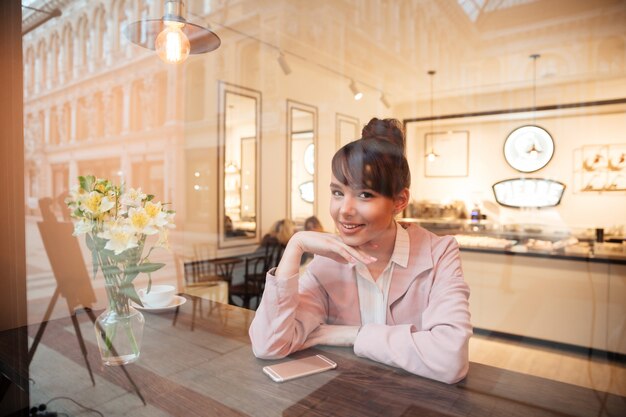 Lächelnde hübsche junge Frau, die drinnen am Kaffeetisch sitzt