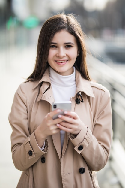 Lächelnde hübsche junge Modelltext eine Nachricht auf ihrem Telefon draußen
