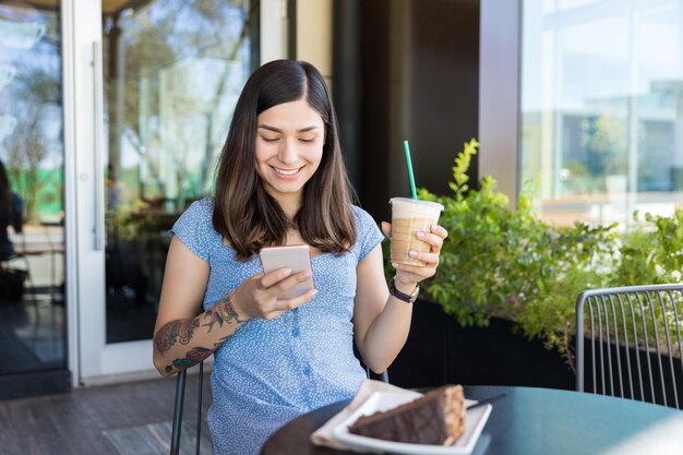 Lächelnde Influencer-Messaging auf dem Handy beim Kaffeetrinken im Café