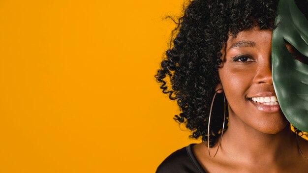 Lächelnde junge Afroamerikanerfrau mit Blatt auf farbigem Hintergrund