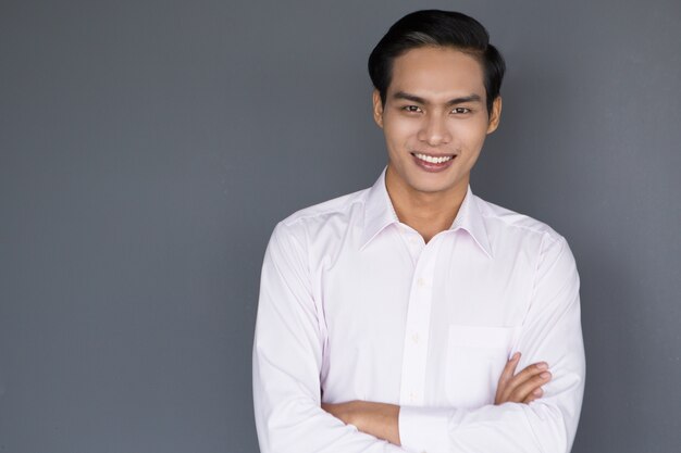 Lächelnde junge asiatische Geschäftsmann mit den gekreuzten Armen
