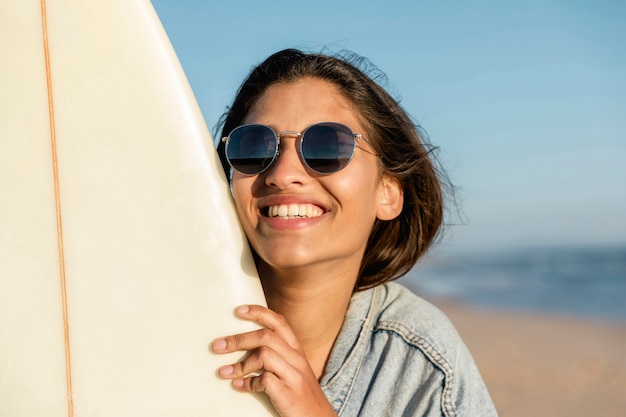 Lächelnde junge Frau am Strand mit Surfbrett