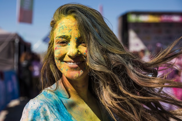 Lächelnde junge Frau bedeckte ihr Gesicht mit der holi Farbe, die Kamera betrachtet