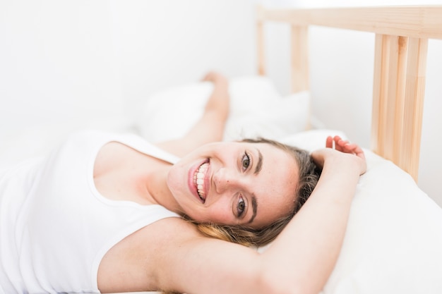 Lächelnde junge Frau, die auf Bett liegt