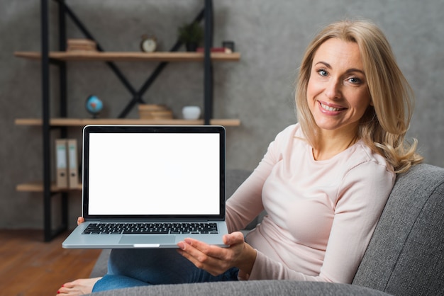 Lächelnde junge Frau, die auf dem Sofa zeigt ihre Laptopanzeige sitzt