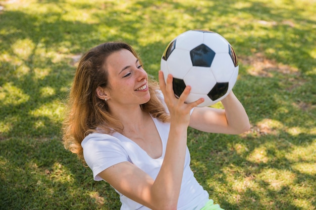 Kostenloses Foto lächelnde junge frau, die auf gras mit fußball sitzt