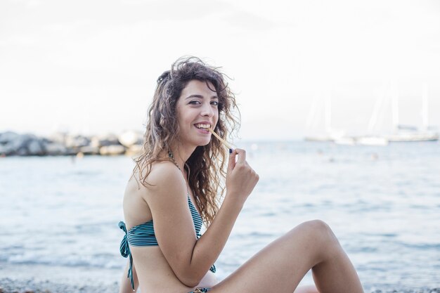 Lächelnde junge Frau, die Brotsteuerknüppel am Strand isst