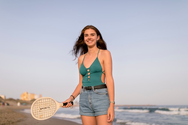 Lächelnde junge Frau, die den Schläger steht am Strand hält