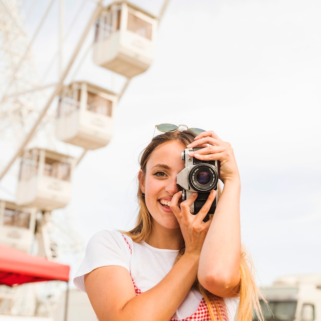 Lächelnde junge Frau, die Fotos mit Kamera am Vergnügungspark macht