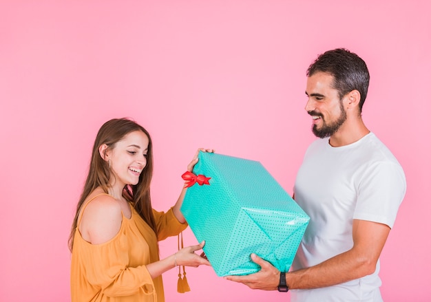 Lächelnde junge Frau, die Geschenk vom Mann gegen rosa Hintergrund nehmend gibt