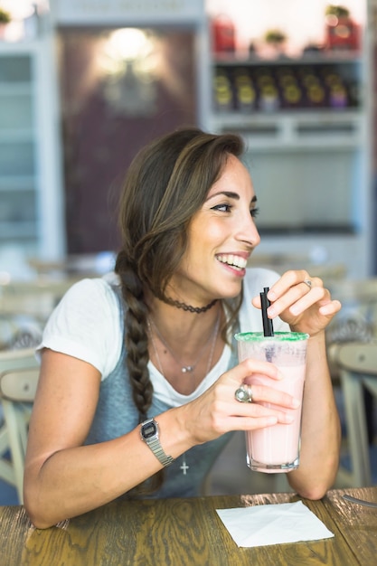 Lächelnde junge Frau, die Glas Milchshaken mit Seidenpapier auf Tabelle hält