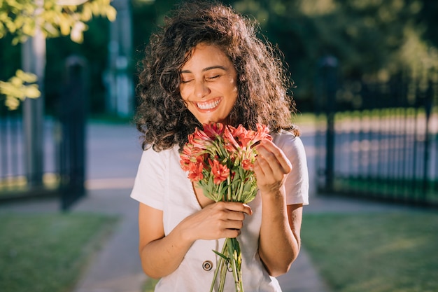 Lächelnde junge Frau, die in der Hand Blumenblumenstrauß hält