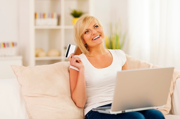Lächelnde junge Frau, die Laptop verwendet und Kreditkarte hält