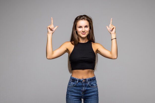 Lächelnde junge Frau, die mit dem Finger nach oben auf grauem Hintergrund zeigt