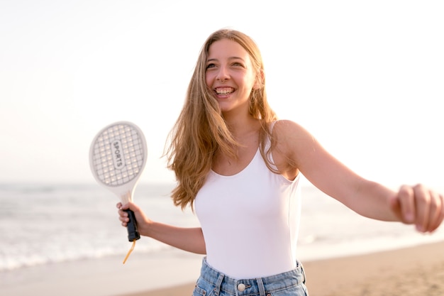 Lächelnde junge Frau, die mit Schläger am Strand spielt