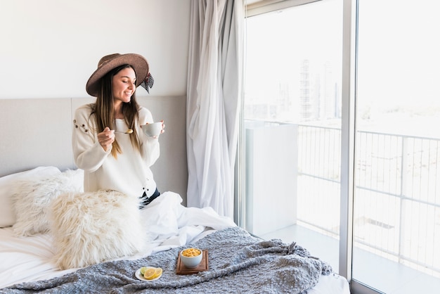 Lächelnde junge Frau, die morgens das gesunde Frühstück auf Bett genießt