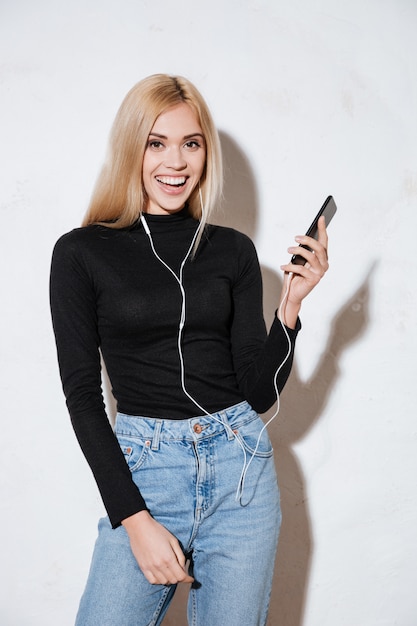 Lächelnde junge Frau, die Musik mit Kopfhörern und Handy hört