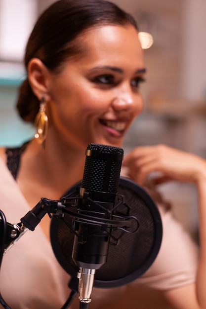 Lächelnde junge Frau, die Podcast-Aufnahme für Online-Show im Heimstudio macht