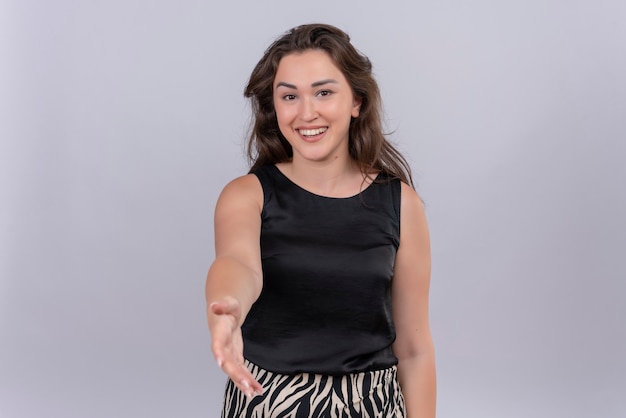 Lächelnde junge Frau, die schwarzes Unterhemd trägt, streckte Hand auf weißer Wand aus