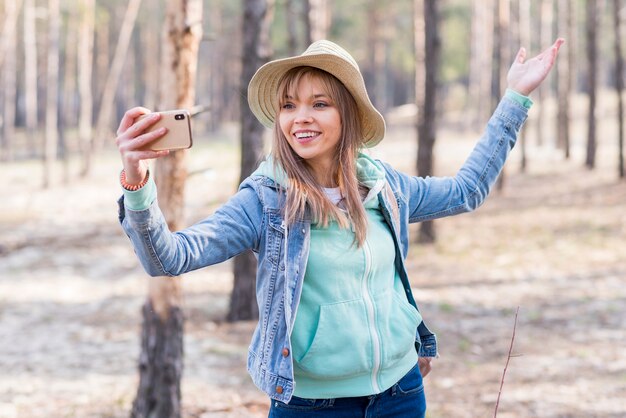 Lächelnde junge Frau, die selfie am Handy im Wald nimmt