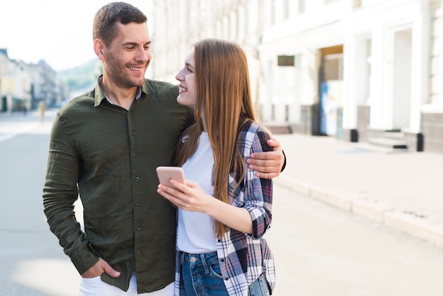 Lächelnde junge Frau, die Smartphone hält und ihren Freund auf Straße betrachtet
