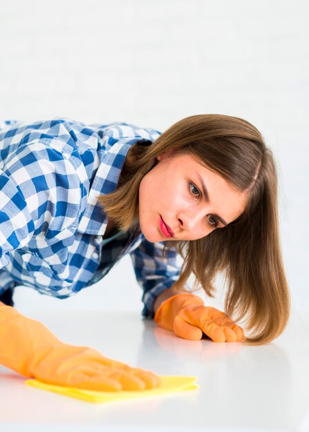 Lächelnde junge Frau, die Staub unter Verwendung des Staubtuchs abwischt