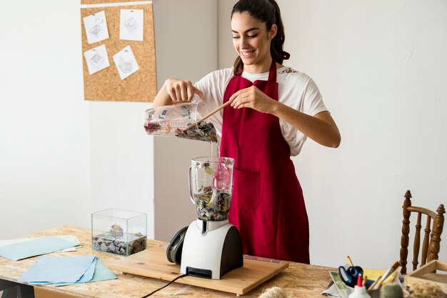 Lächelnde junge Frau, die Vorbereitung für das Schleifen von Papierstücken in der Mischmaschine macht