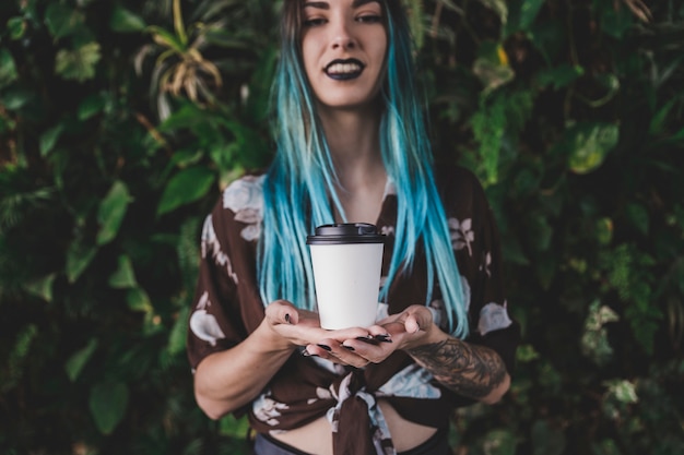 Lächelnde junge Frau, die Wegwerfkaffeetasse in zwei Händen hält