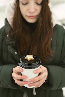 Lächelnde junge frau hält eine tasse heißen tee oder kaffee mit lebkuchen