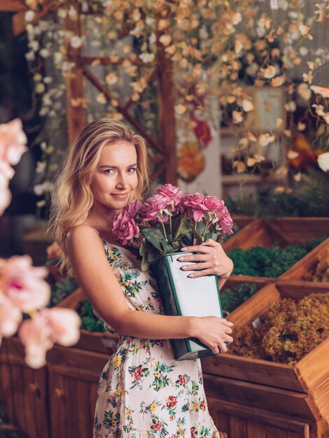 Lächelnde junge Frau im Blumenkleid, das rosa Rosen im Behälter hält