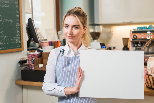 Lächelnde junge Frau in der Kaffeestube, die leeres weißes Segeltuch zeigt