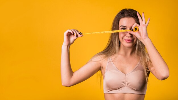 Lächelnde junge Frau in der Sportkleidung, die messendes Band hält