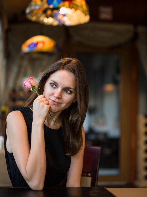 Lächelnde junge Frau mit Blume am Tisch