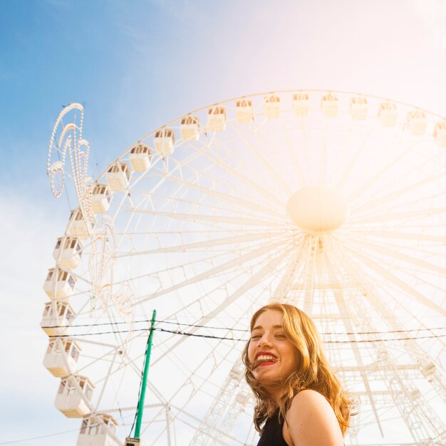 Lächelnde junge Frau vor weißem Riesenrad gegen blauen Himmel